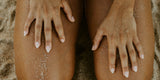 Close-up of sandy hands resting on sun-kissed legs at the beach, showing textured skin and natural nails.